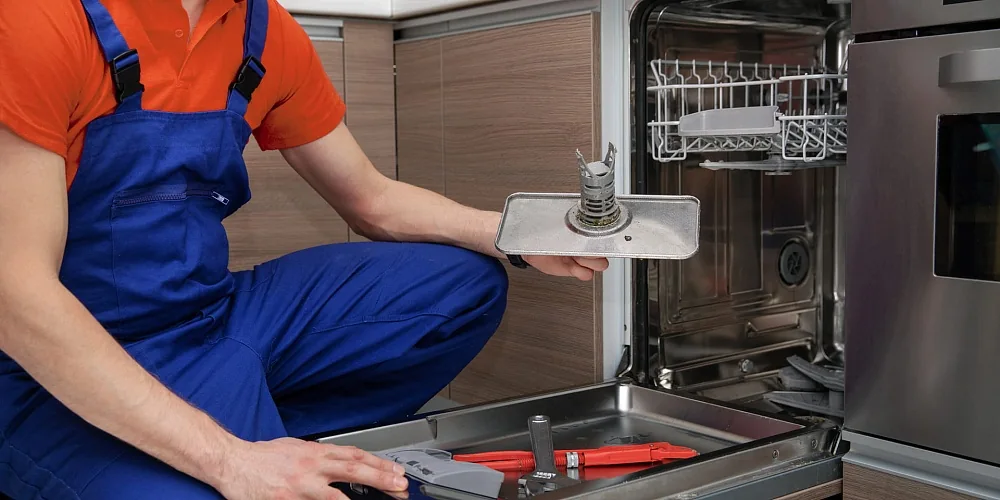 Technician holding a dishwasher filter assembly beside an open appliance