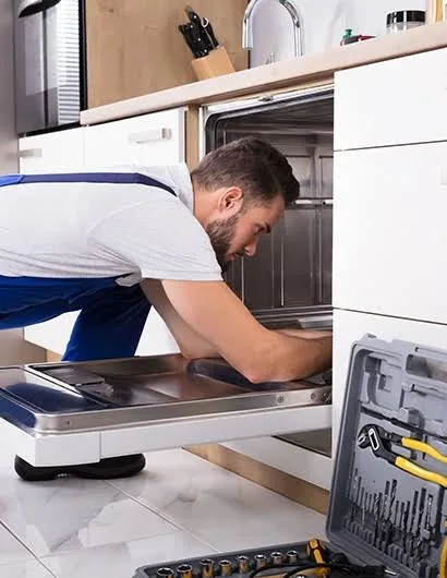 Technician working inside an open dishwasher with a tool case nearby