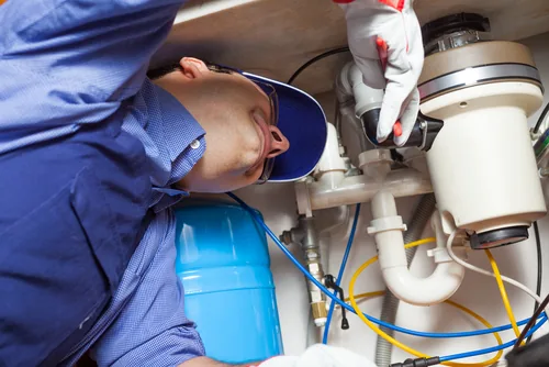 Technician inspecting plumbing and a garbage disposal beneath a sink