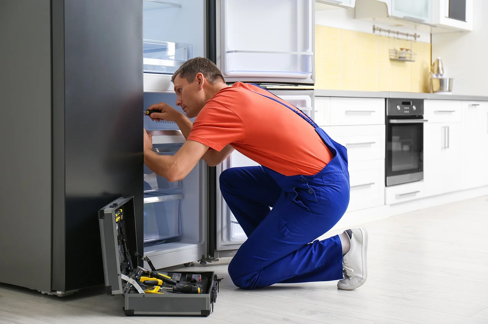 Technician using a screwdriver while inspecting a refrigerator in a residential kitchen