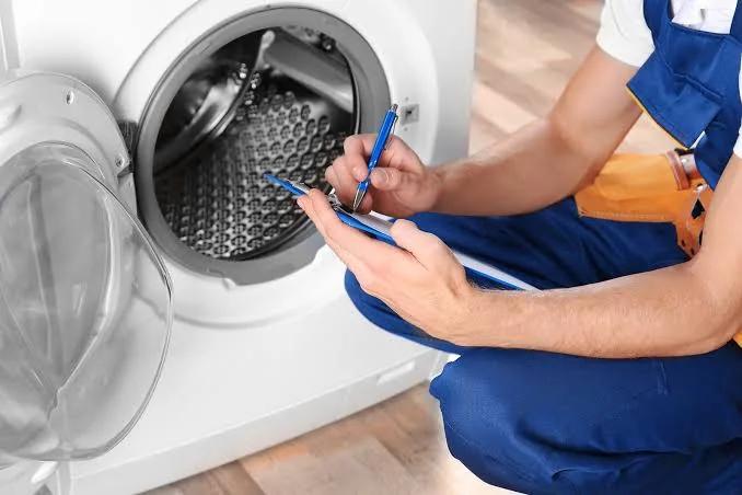 Technician recording observations beside an open front-loading washer